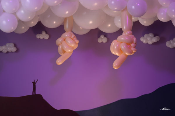 Defiance balloon sculpture of large hands in clouds flipping off small man returning the finger