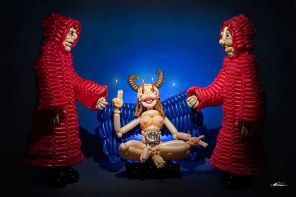 balloon sculpture of woman with baphomet elements and candles in eyes sitting between two hooded figures in red