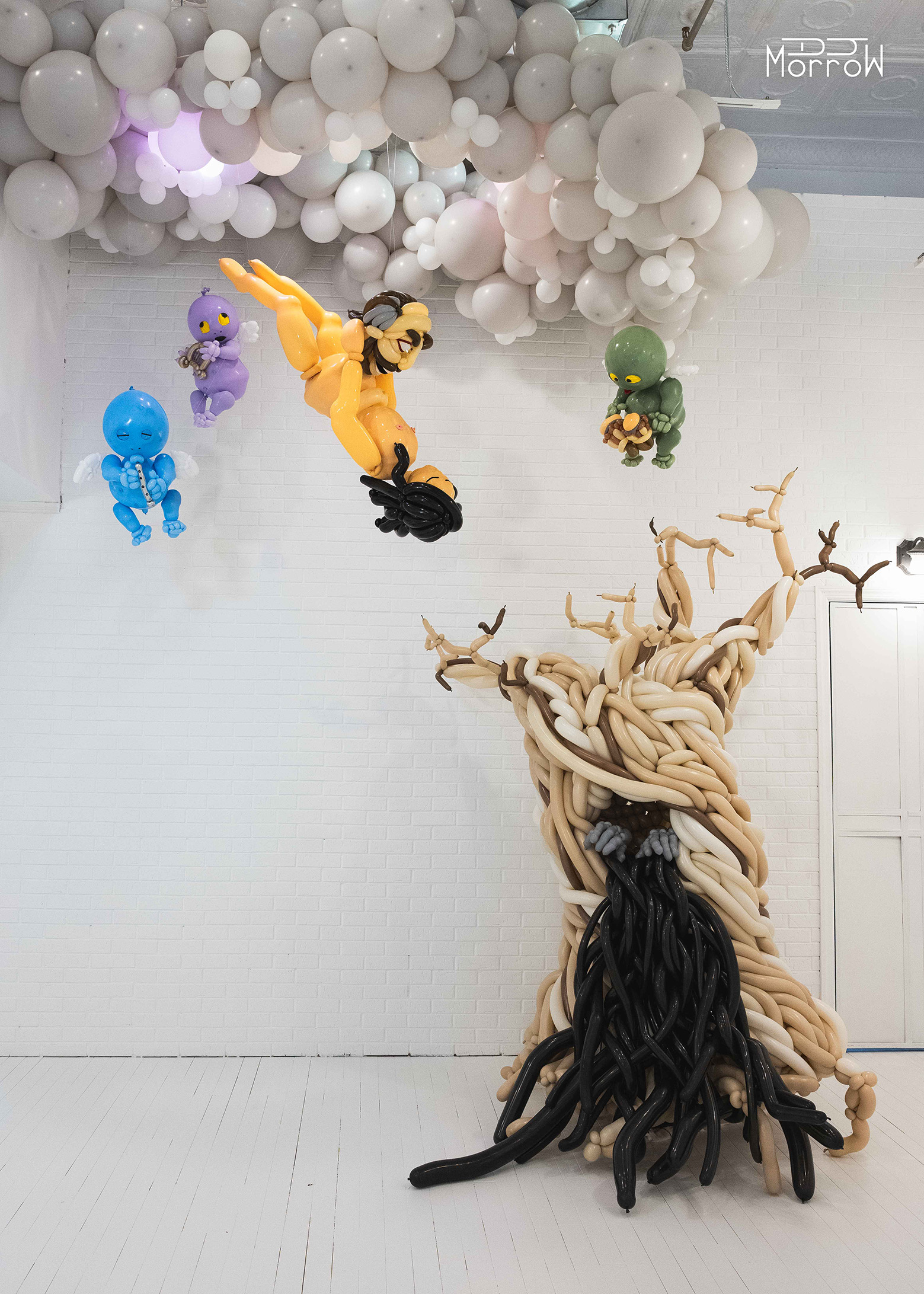 Ode to a Falling Star balloon installation falling figure from clouds with multicolored floating imps playing instruments holding angry head with dead tree on floor oozing black with desiccated hands