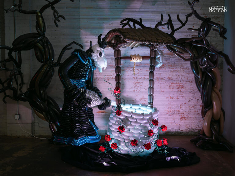 the lightbringer robed skull figure pouring light into well covered in roses and thorns balloon sculpture